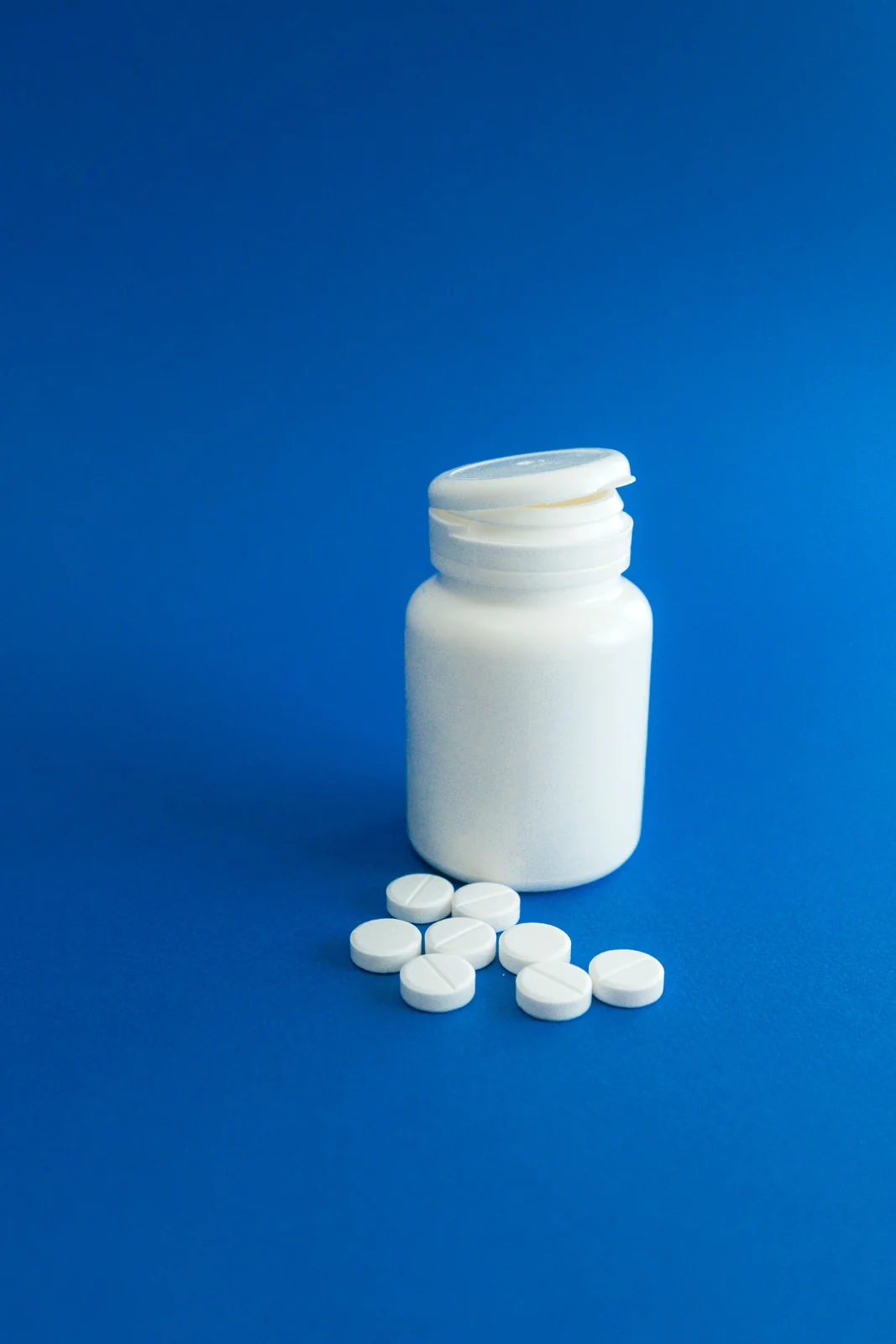 An open bottle with tablets on a plain background